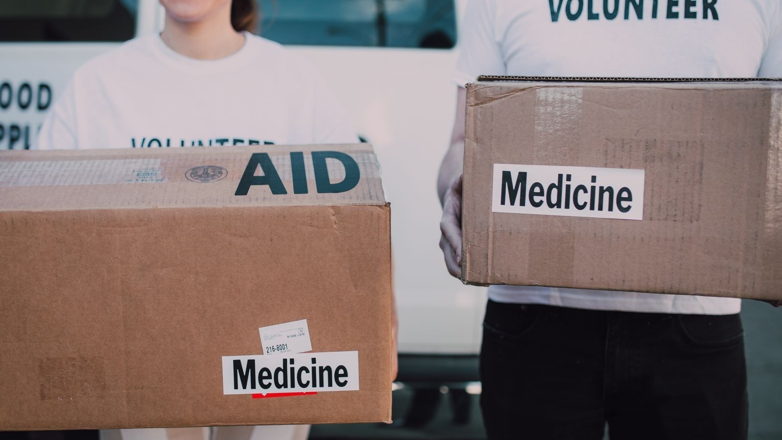 Deux bénévoles portant des cartons de dons étiquetés Aide et Médicaments