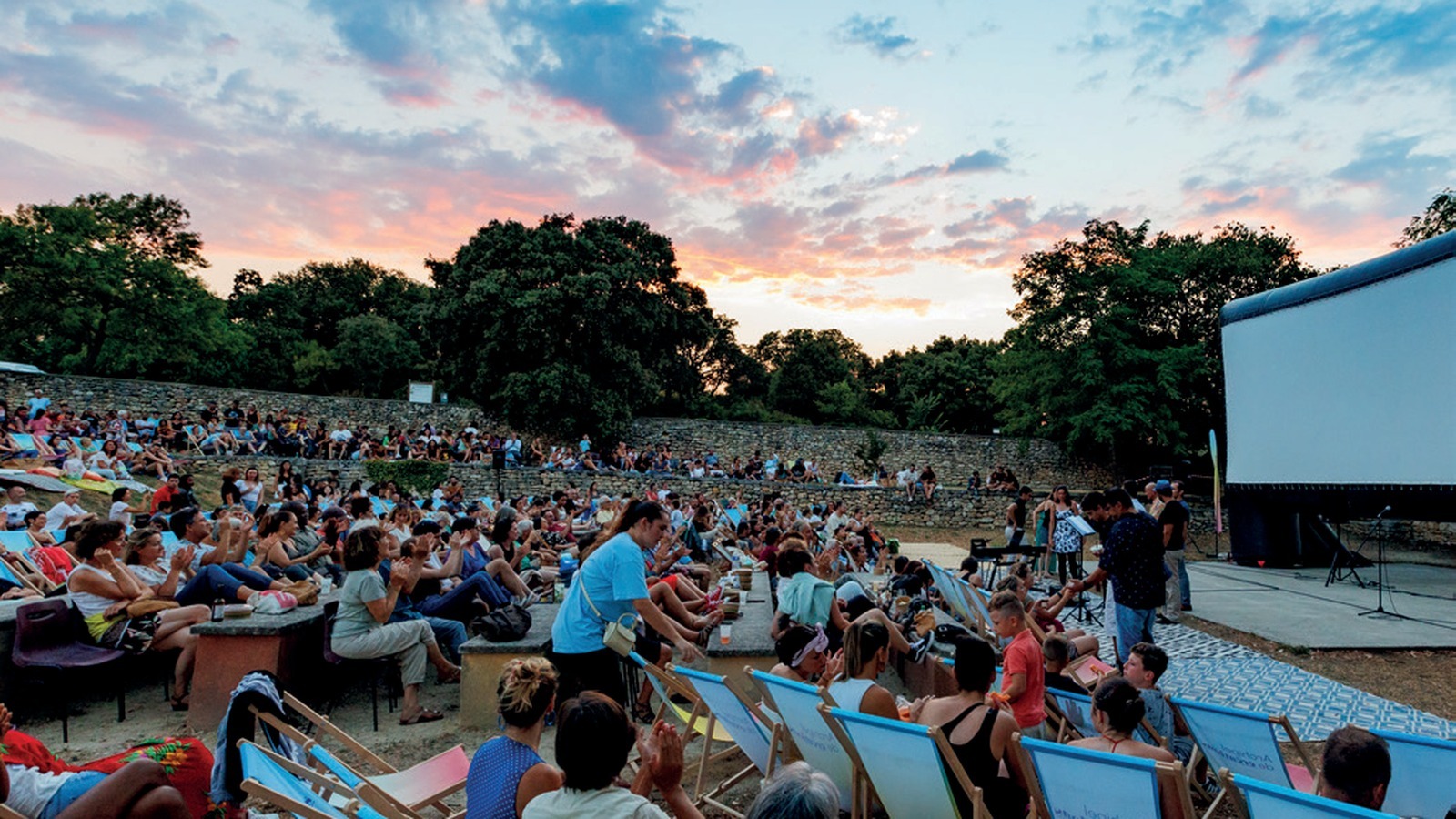 Public installé dans des transats devant l'écran géant du festival Cinéma sous les étoiles au coucher du soleil