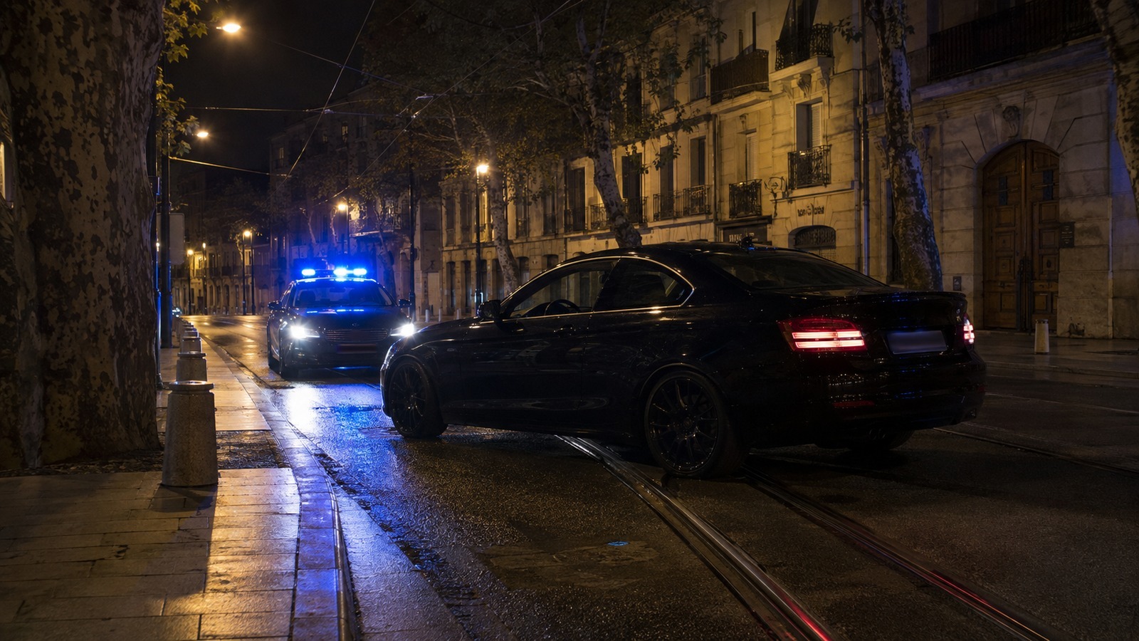 Voiture de sport immobilisée sur les rails du tramway la nuit, véhicule de police gyrophares allumés derrière