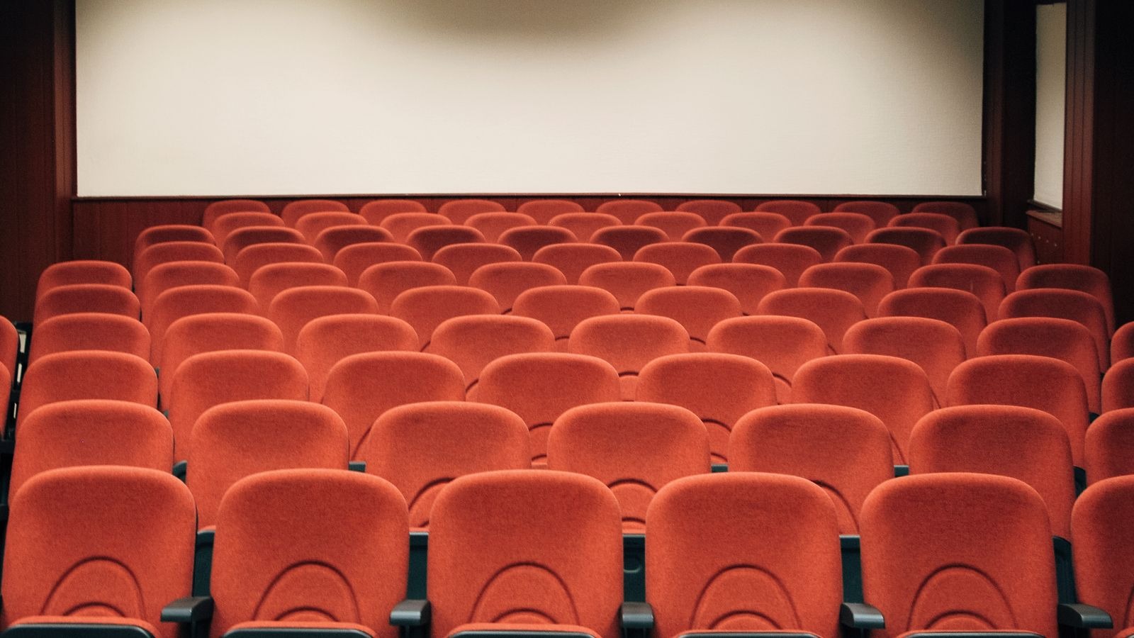 Salle de cinéma vide aux fauteuils rouges face à un écran blanc